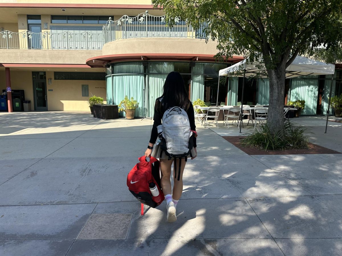 A student athlete walking into campus while carrying her volleyball backpack.