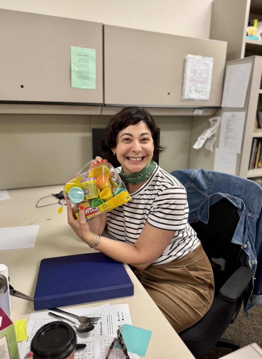 Dr. Fine in her office, holding a brand-new case of Play-Doh for her students. 