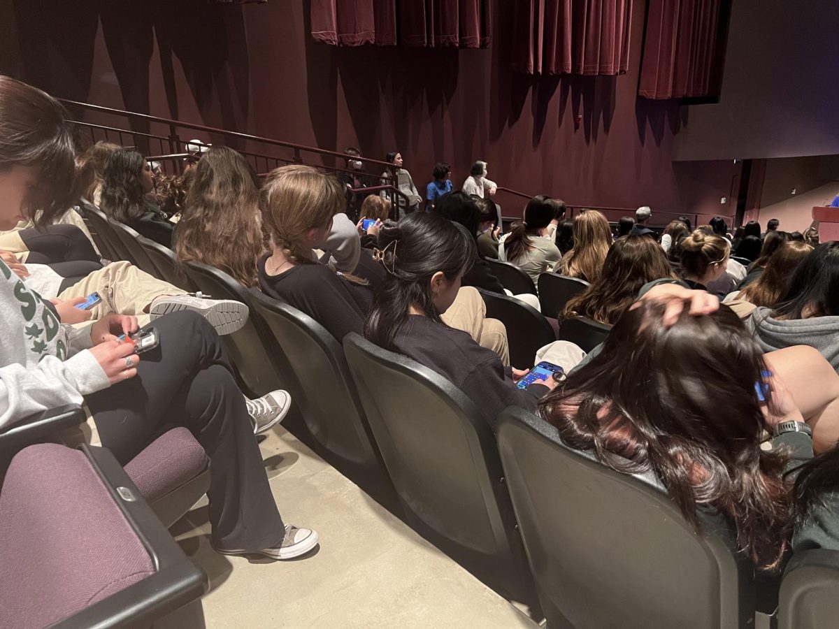 At least four students on their phones during the start of an assembly.