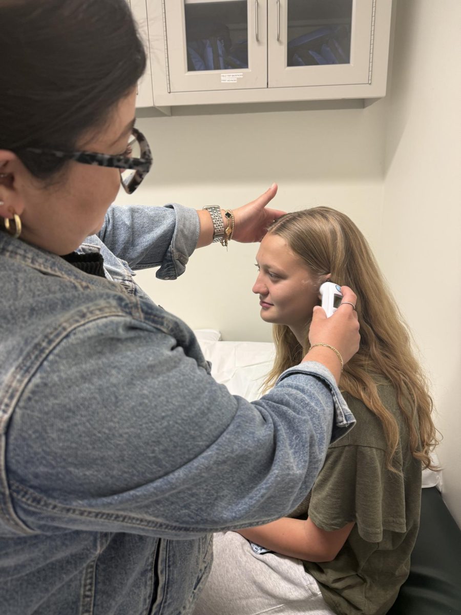 Bennet T. '28 gets her temperature taken by Ms. Beltran.